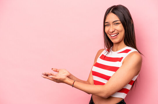 Young hispanic woman isolated on pink background holding a copy space on a palm.