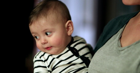 Mother holding baby casually indoors while talking. Parent holds infant toddler