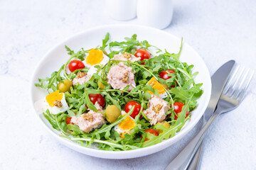 Salad with tuna, arugula, tomatoes, olives and eggs in a white plate. A traditional dish. Close-up.