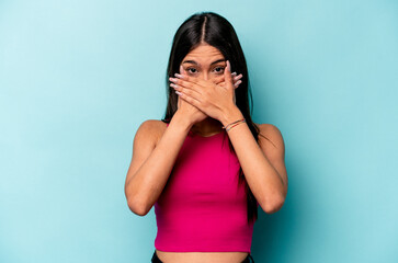 Young hispanic woman isolated on blue background covering mouth with hands looking worried.