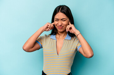 Young hispanic woman isolated on blue background covering ears with fingers, stressed and desperate by a loudly ambient.