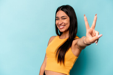 Fototapeta premium Young hispanic woman isolated on blue background joyful and carefree showing a peace symbol with fingers.