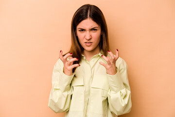 Young hispanic woman isolated on beige background upset screaming with tense hands.