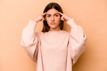 Young hispanic woman isolated on beige background focused on a task, keeping forefingers pointing head.