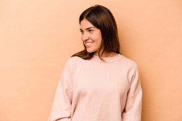 Young hispanic woman isolated on beige background laughs happily and has fun keeping hands on stomach.