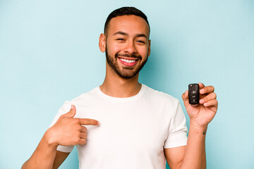 Young hispanic man holding car keys isolated on blue background person pointing by hand to a shirt...