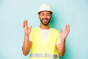 Young laborer hispanic man isolated on blue background receiving a pleasant surprise, excited and...