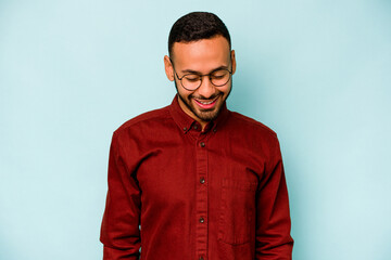 Obraz premium Young hispanic man isolated on blue background laughs and closes eyes, feels relaxed and happy.