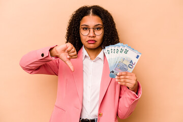Young African American business woman holding banknotes isolated on beige background showing a...