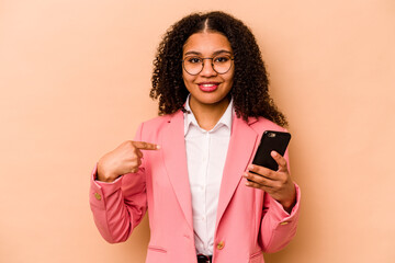 Young African American woman holding mobile phone isolated on beige background person pointing by hand to a shirt copy space, proud and confident