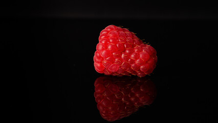 raspberry on black background with reflection on black bottom