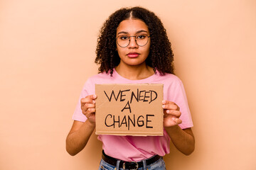 Young African american woman holding we need a change placard isolated on beige background