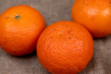 Three tangerines on a table covered with a homespun cloth with a rough texture