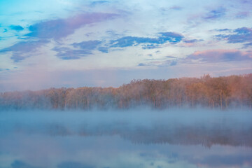 Foggy spring landscape at dawn of the shoreline of Deep Lake with mirrored reflections in calm water, Yankee Springs State Park, Michigan, USA