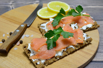 healthy sandwiches with salmon and soft cheese on cutting board decorated with parsley and lemon