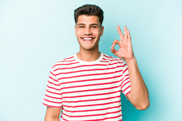 Young caucasian man isolated on blue background cheerful and confident showing ok gesture.