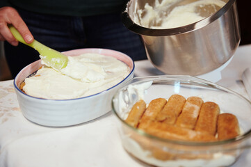 Close-up. Chef's hand putting mixed mascarpone and whipped cream cheese cream on the cake while making tiramisu - traditional Italian dessert at home