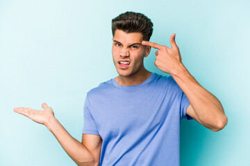 Young caucasian man isolated on blue background showing a disappointment gesture with forefinger.