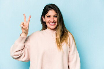 Young caucasian woman isolated on blue background joyful and carefree showing a peace symbol with fingers.
