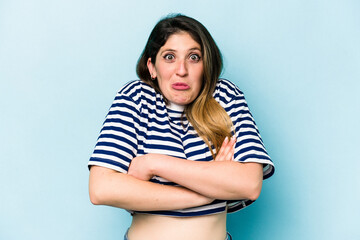 Young caucasian woman isolated on blue background shrugs shoulders and open eyes confused.