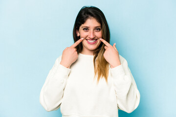 Young caucasian woman isolated on blue background smiles, pointing fingers at mouth.