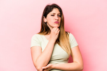 Young caucasian woman isolated on pink background suspicious, uncertain, examining you.