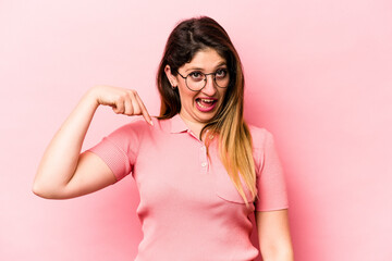 Young caucasian woman isolated on pink background person pointing by hand to a shirt copy space, proud and confident