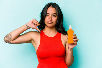 Young hispanic woman holding sun cream isolated on blue background feels proud and self confident, example to follow.