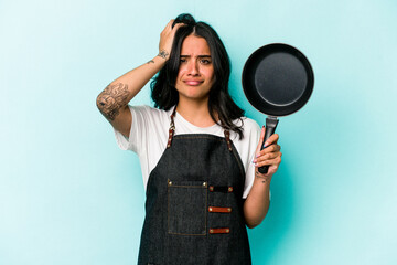 Young hispanic cooker woman holding frying pan isolated on blue background being shocked, she has...