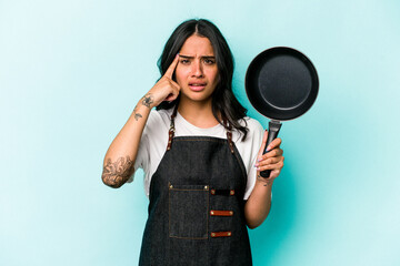 Young hispanic cooker woman holding frying pan isolated on blue background showing a disappointment...