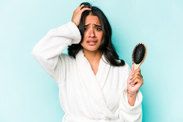 Young hispanic woman holding hairbrush isolated on blue background being shocked, she has remembered important meeting.