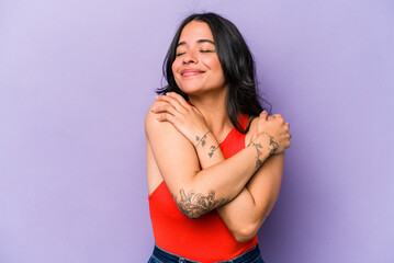 Young hispanic woman isolated on purple background hugs, smiling carefree and happy. - obrazy, fototapety, plakaty