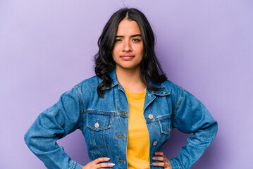Young hispanic woman isolated on purple background frowning face in displeasure, keeps arms folded.