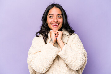 Young hispanic woman isolated on purple background keeps hands under chin, is looking happily aside.