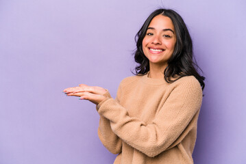 Young hispanic woman isolated on purple background holding a copy space on a palm.