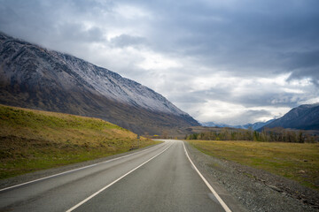 Road in the mountains of southern Altai with view on snow tops and spring forest, Russia