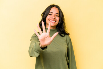 Young hispanic woman isolated on yellow background smiling cheerful showing number five with fingers.