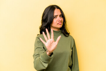 Young hispanic woman isolated on yellow background rejecting someone showing a gesture of disgust.