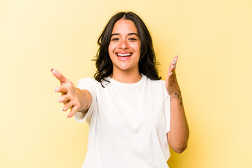 Young hispanic woman isolated on yellow background feels confident giving a hug to the camera.