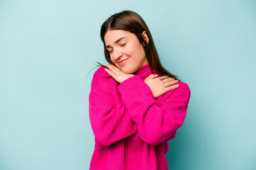 Young caucasian woman isolated on blue background hugs, smiling carefree and happy.