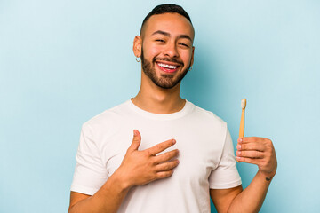Fototapeta Young hispanic man brushing teeth isolated on blue background laughs out loudly keeping hand on chest. obraz