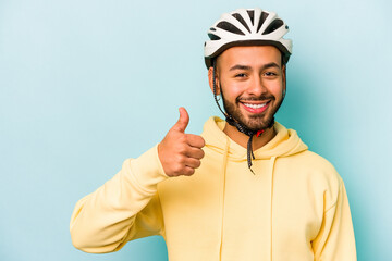 Young hispanic man wearing helmet isolated on blue background smiling and raising thumb up