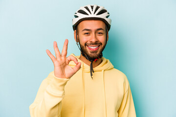 Young hispanic man wearing helmet isolated on blue background cheerful and confident showing ok gesture.