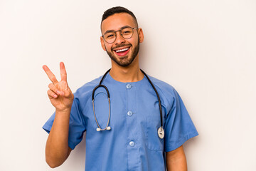 Young hispanic nurse man isolated on white background joyful and carefree showing a peace symbol with fingers.