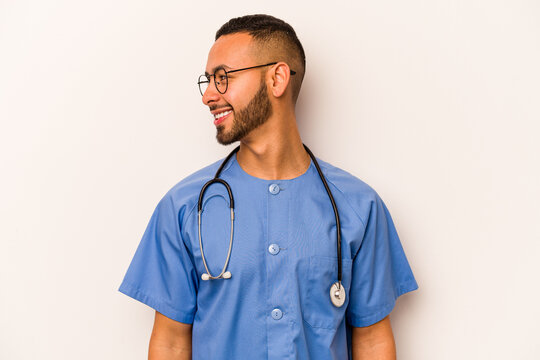 Young hispanic nurse man isolated on white background looks aside smiling, cheerful and pleasant.