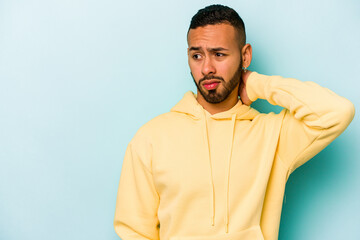 Young hispanic man isolated on blue background touching back of head, thinking and making a choice.