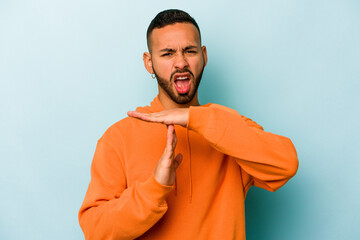 Young hispanic man isolated on blue background showing a timeout gesture.