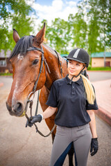 Obraz premium Lovely young woman wearing helmet stroking to her brown horse