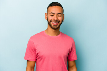 Young hispanic man isolated on blue background laughs and closes eyes, feels relaxed and happy.