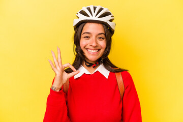 Young student hispanic woman wearing a bike helmet isolated on yellow background cheerful and confident showing ok gesture.